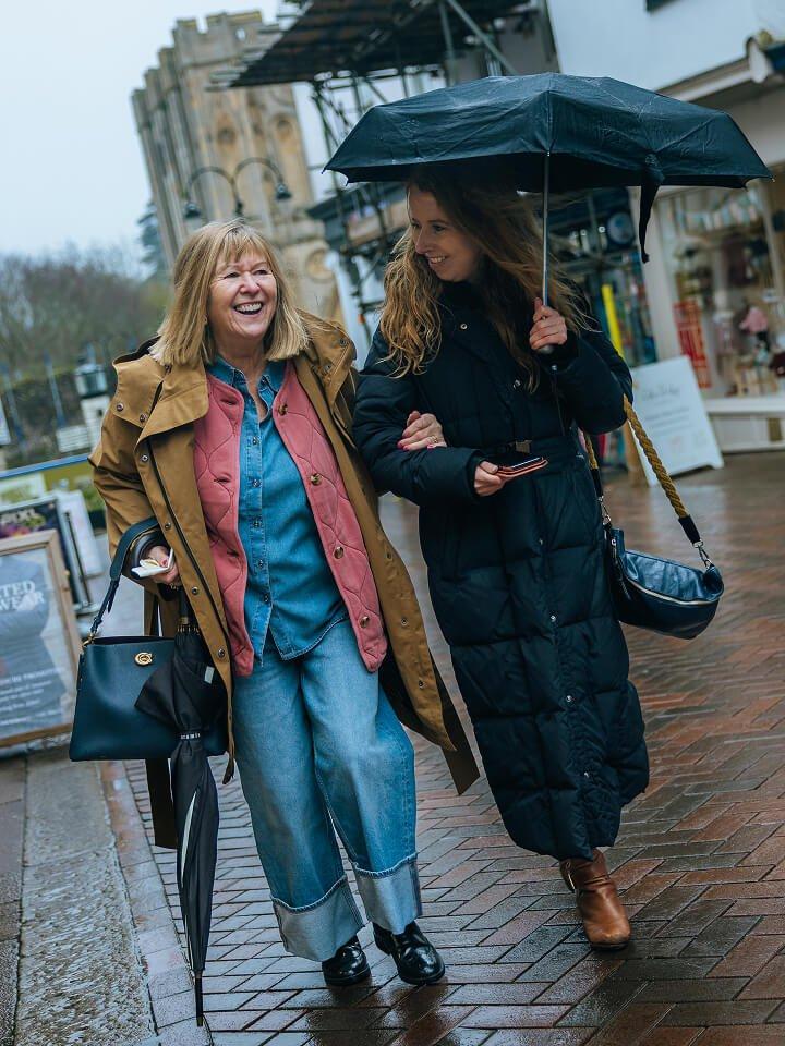 two women walking down a brick sidewalk holding an umbrella